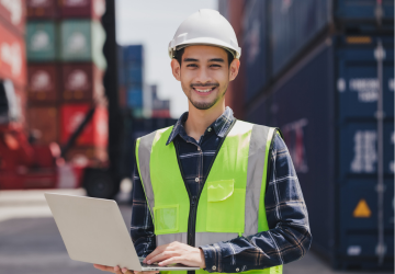Portrait engineer male wearing safety vest and hard helmet hand holding laptop computer standing in front of container box on site Cargo freight ship for import and export.